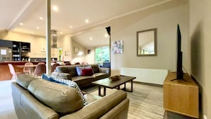 A modern living room with a sofa, coffee table, and a television. There is a kitchen in the background.