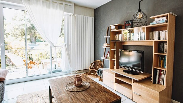 Una sala moderna con un televisor grande, estanterías de madera, una mesa de comedor y vistas a un jardín a través de amplios ventanales.