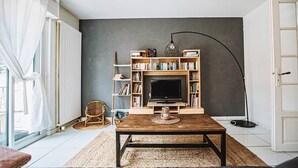 Una sala de estar con televisor, estanterías, una mesa de centro, una silla y una lámpara.