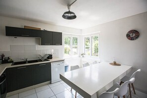 Uma cozinha moderna com armários escuros, bancada branca e uma ilha grande com cadeiras.