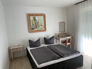 Een slaapkamer met een bed, nachtkastjes, een dressoir, een spiegel en een schilderij aan de muur.
