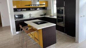 Une cuisine moderne dotée d’un îlot central, d’appareils électroménagers en acier inoxydable et d’une palette de couleurs noir et jaune.