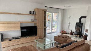 Un salon moderne doté d’un téléviseur à écran plat, d’un canapé en cuir, d’une table basse en verre, d’étagères en bois et d’un poêle à bois.