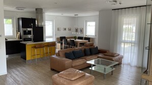 Un salon moderne avec un canapé en cuir marron, une table basse en verre et un coin bar jaune avec des tabourets.