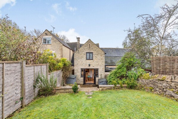 Une maison en pierre avec un petit jardin devant et une clôture en bois.
