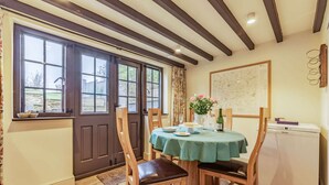 A dining area with a table set for two, a wooden chair, a small refrigerator, and a window with curtains.
