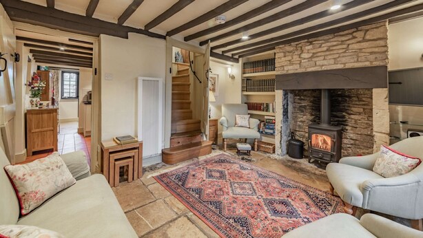 A cozy living room with a stone fireplace, a staircase, and a bookshelf.