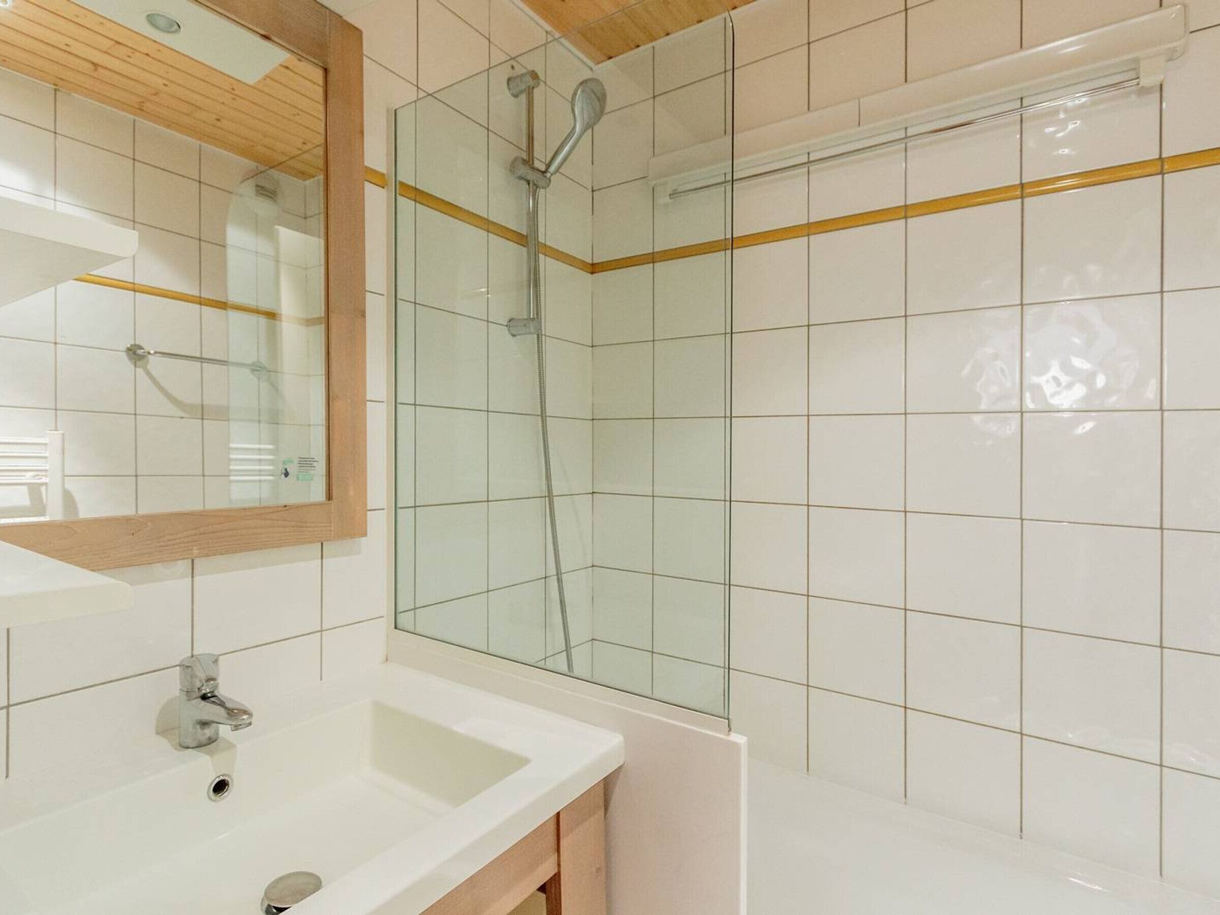 A modern bathroom with a glass shower enclosure, a wooden vanity, and a white sink.