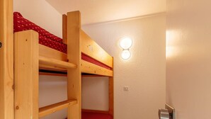 A bunk bed room with a wooden bunk bed, a red mattress, and a wall-mounted light fixture.
