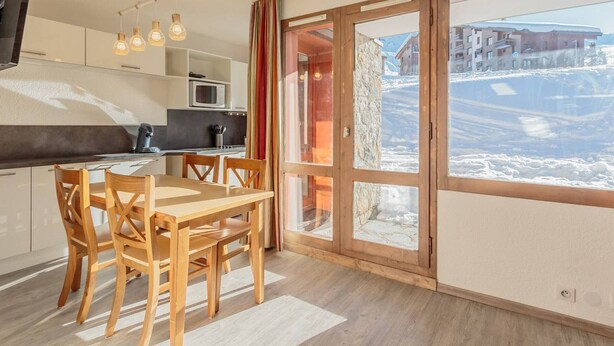 A modern kitchen with a dining area, large windows with a snowy view, and a stone wall.