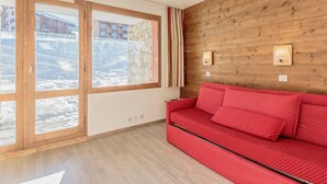 A room with a wooden wall, a red sofa, and a large window with a view of a snowy landscape.