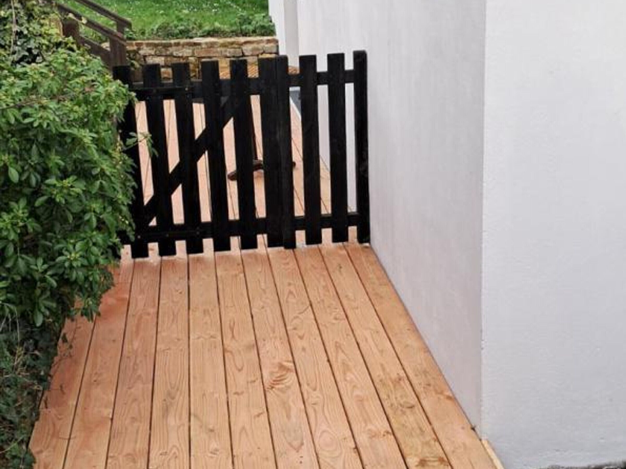 A wooden deck with a black fence, surrounded by greenery.