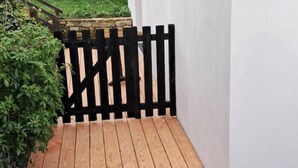 Puinen terassi, jossa on musta aita, ja sen ympärillä on vehreää kasvillisuutta.