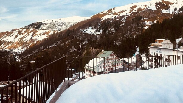 Un paysage de montagne avec des pentes enneigées et un bâtiment doté d’un balcon.