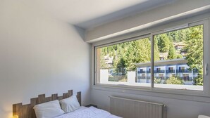 Une chambre avec une grande fenêtre, un lit, une table de chevet et un radiateur.