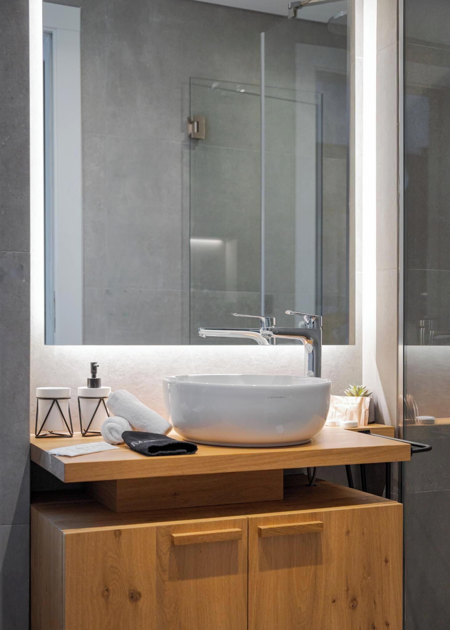 A modern bathroom with a large vessel sink, wooden vanity, and a glass shower enclosure.