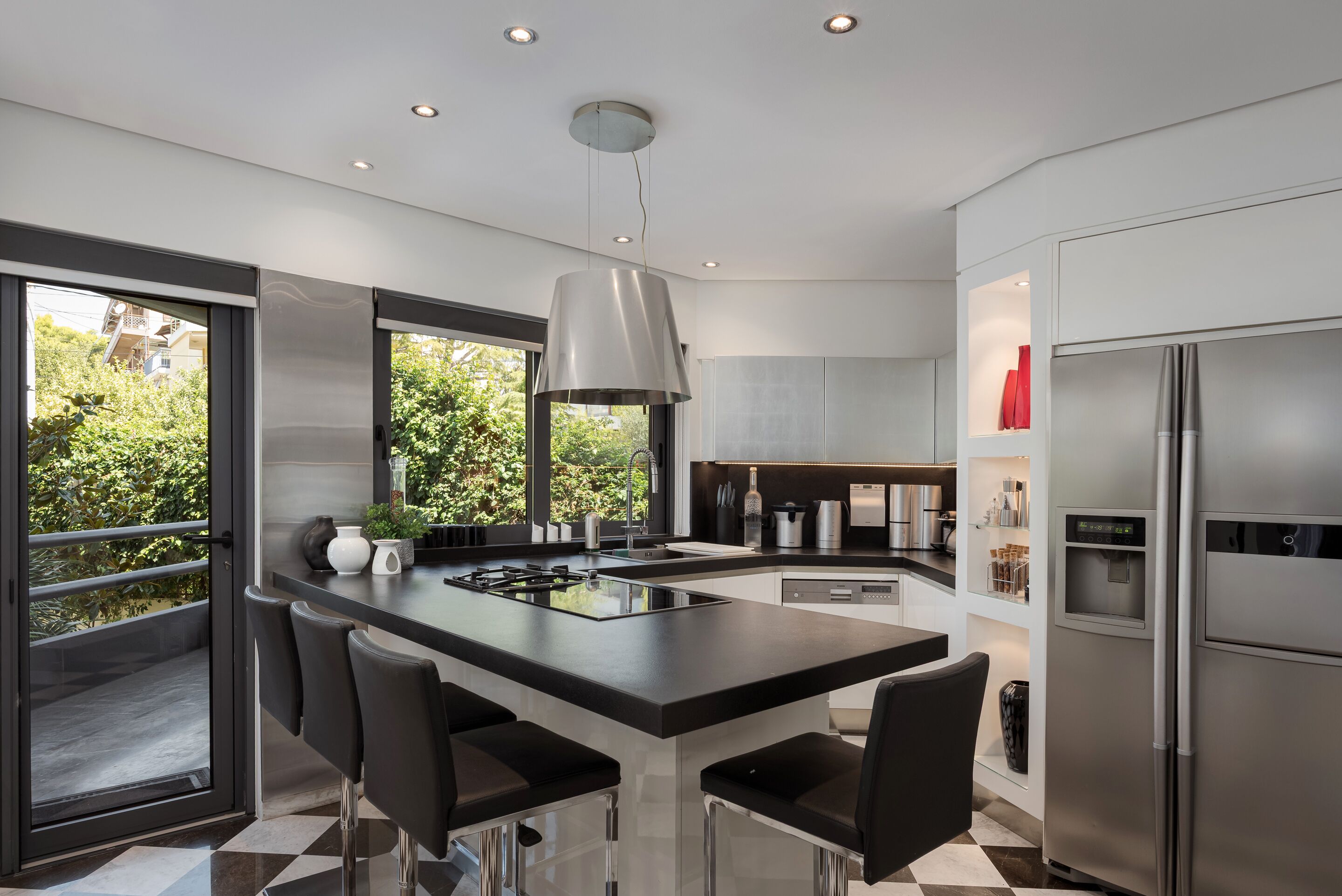 A modern kitchen with a central island, stainless steel appliances, and a view of greenery outside.