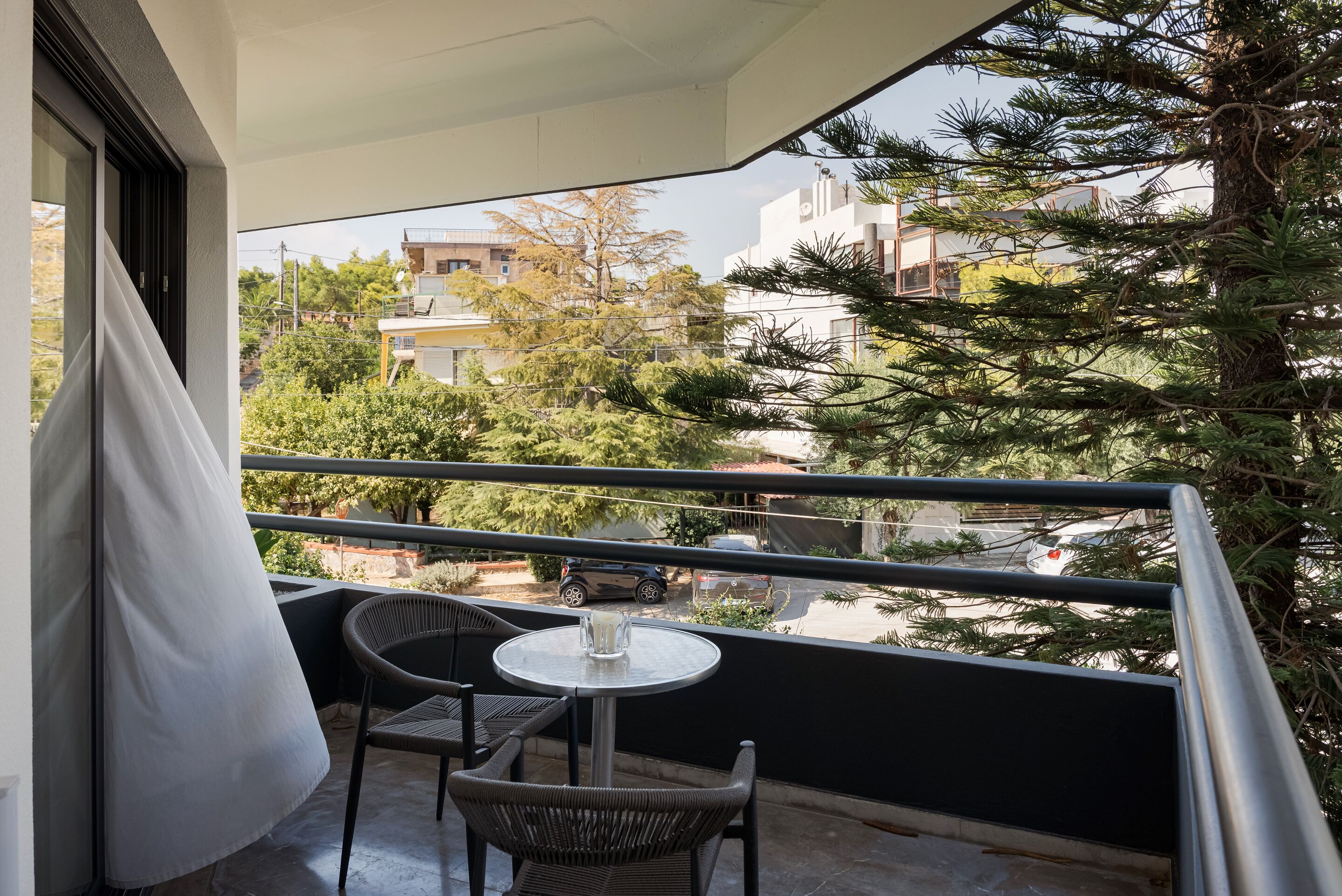 A balcony with a table and chairs, overlooking a residential area with trees and buildings.