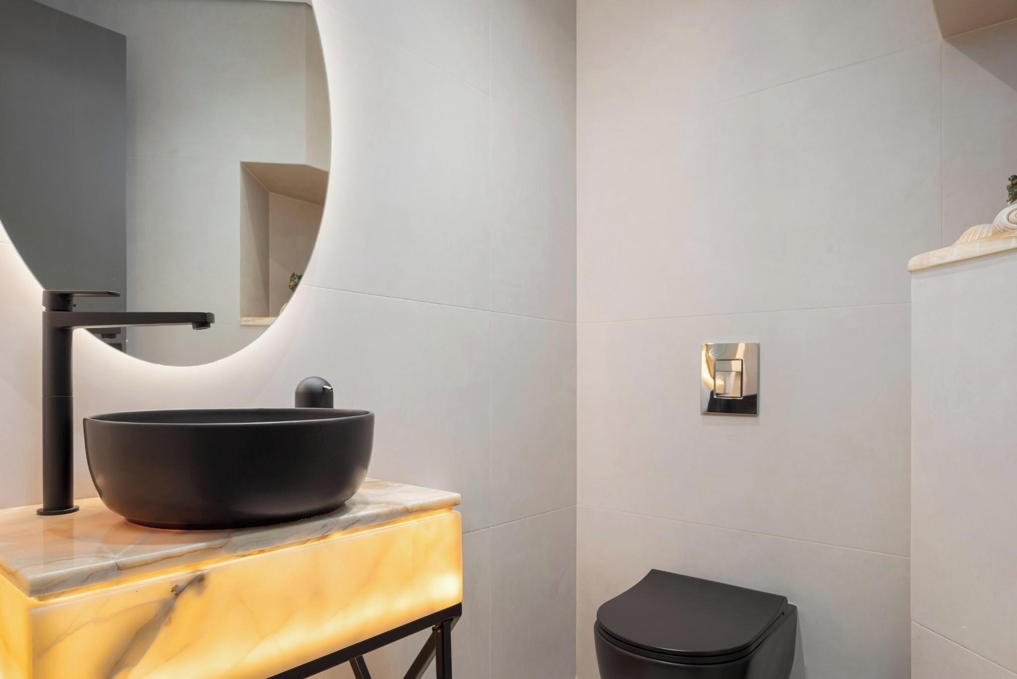 A modern bathroom with a black vessel sink, a marble countertop, a black toilet, and a wall-mounted light fixture.
