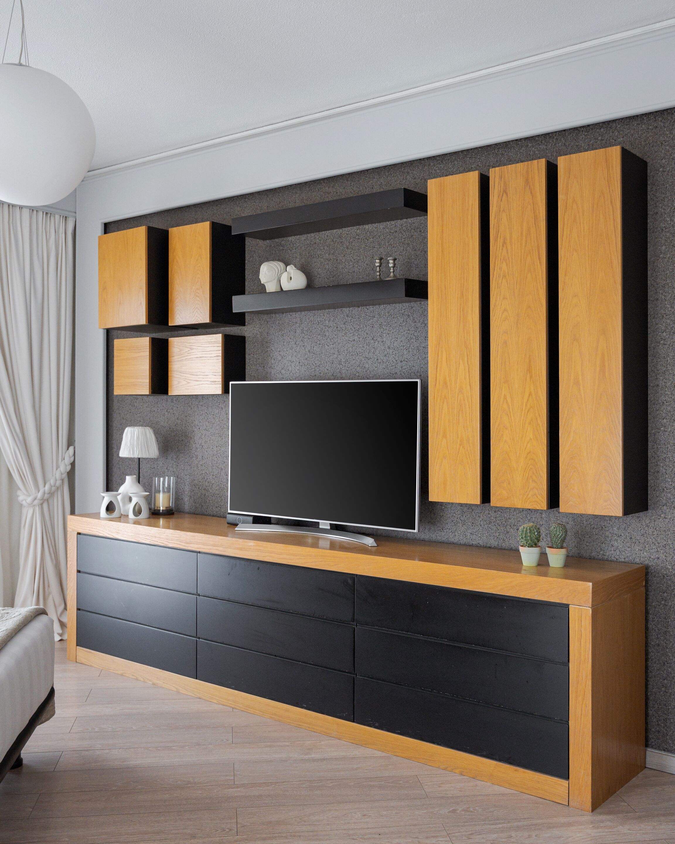 Een moderne woonkamer met een flatscreen televisie, houten kasten en een grijze, gestructureerde muur.