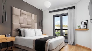 A modern bedroom with a large bed, a wooden nightstand, a grey furry rug, and a view of the outdoors through a window with curtains. - Athenian Riviera Luxurious Villa & Residence (Alimos)