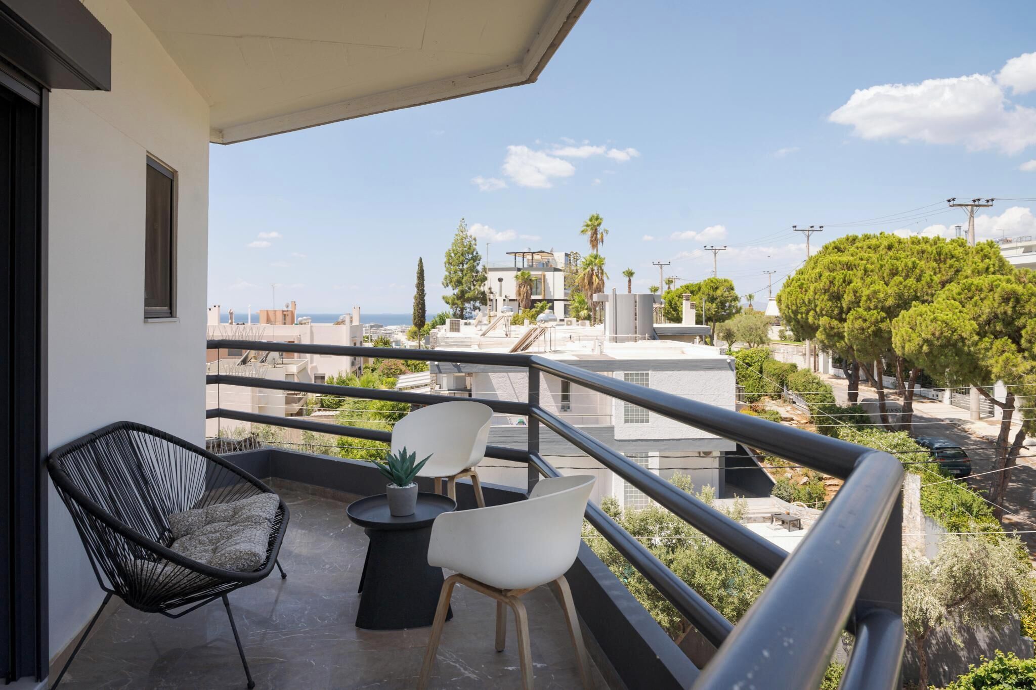 A balcony with two chairs and a small table, overlooking a residential area with trees and buildings.