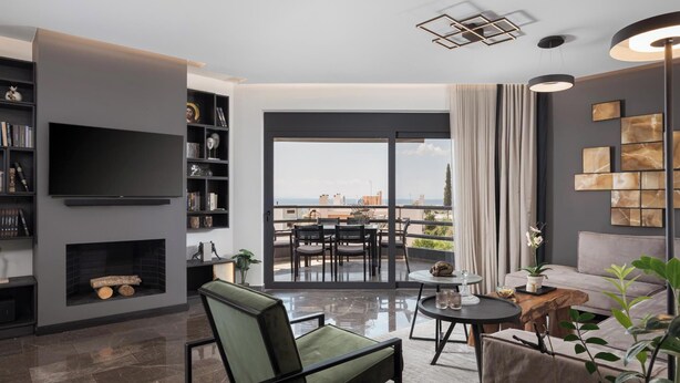 A modern living room with a flat-screen TV, bookshelves, a fireplace, a balcony with a table and chairs, and a view of the city. - Athenian Riviera Luxurious Villa & Residence (Alimos)