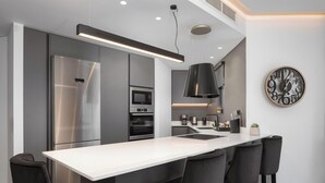 A modern kitchen with a central island, stainless steel appliances, and a black pendant light. - Athenian Riviera Luxurious Villa & Residence (Alimos)