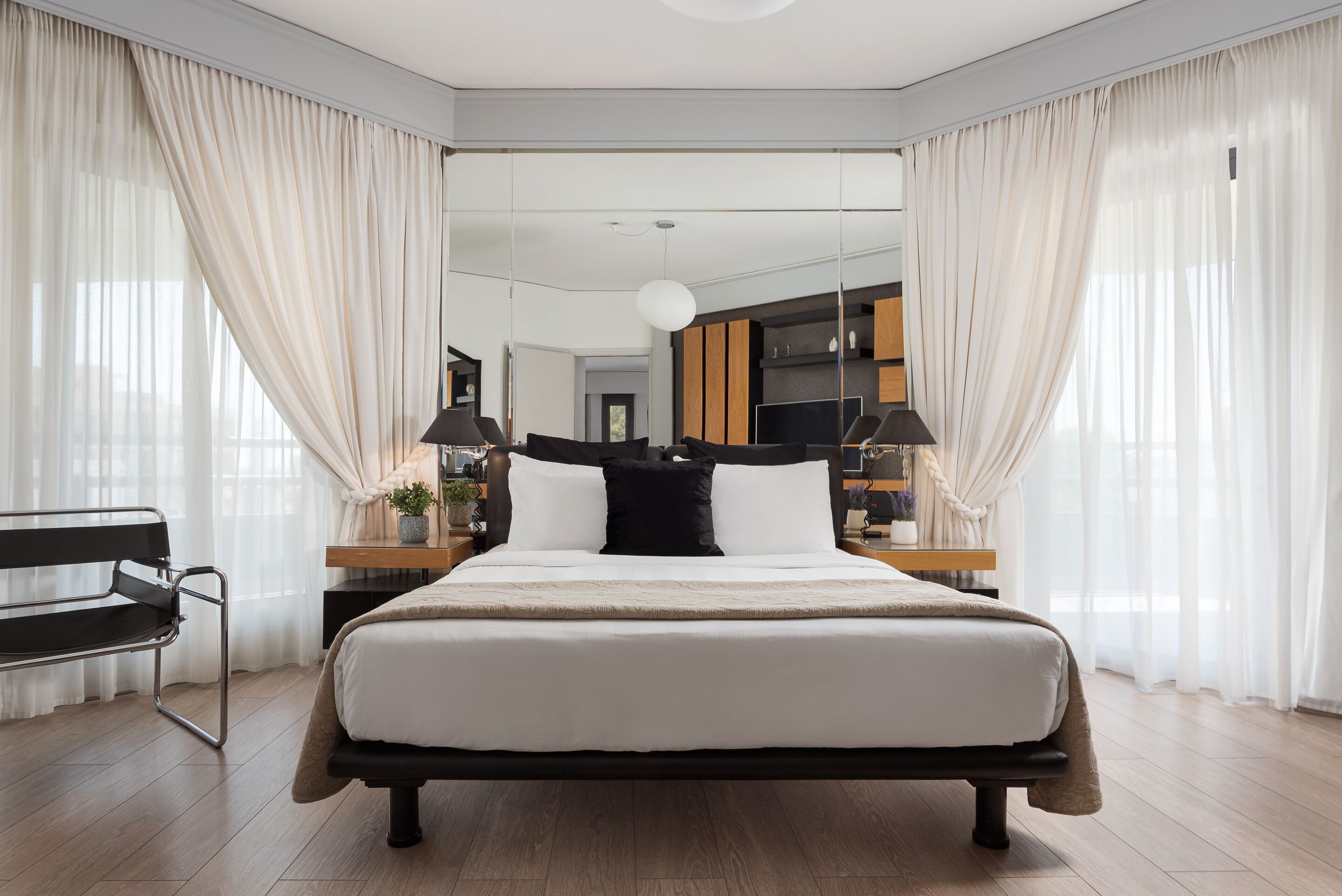 A modern bedroom with a large bed, bedside tables, a bench, and a view into another room.