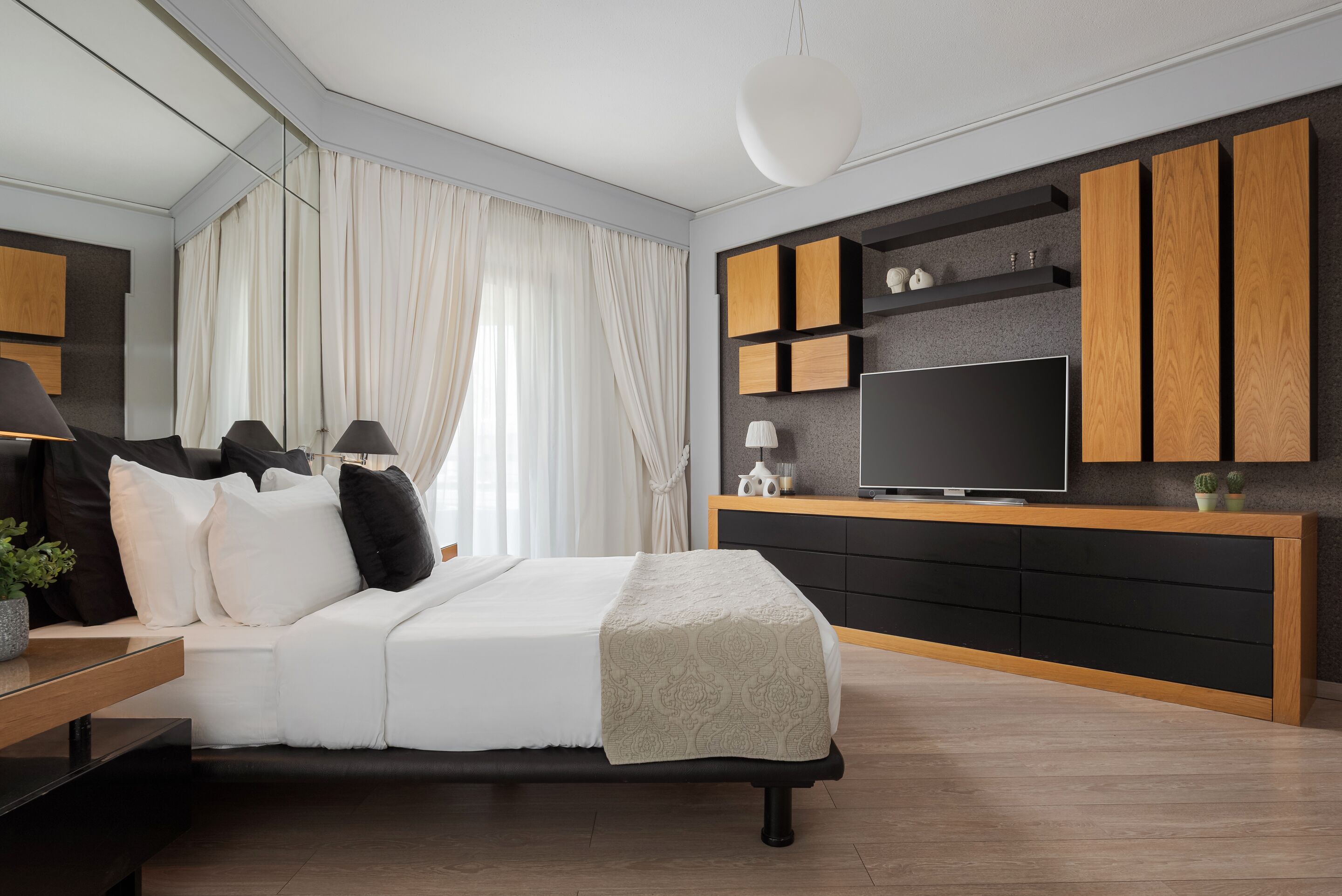 A modern bedroom with a bed, bedside tables, a TV, and built-in wooden cabinets.