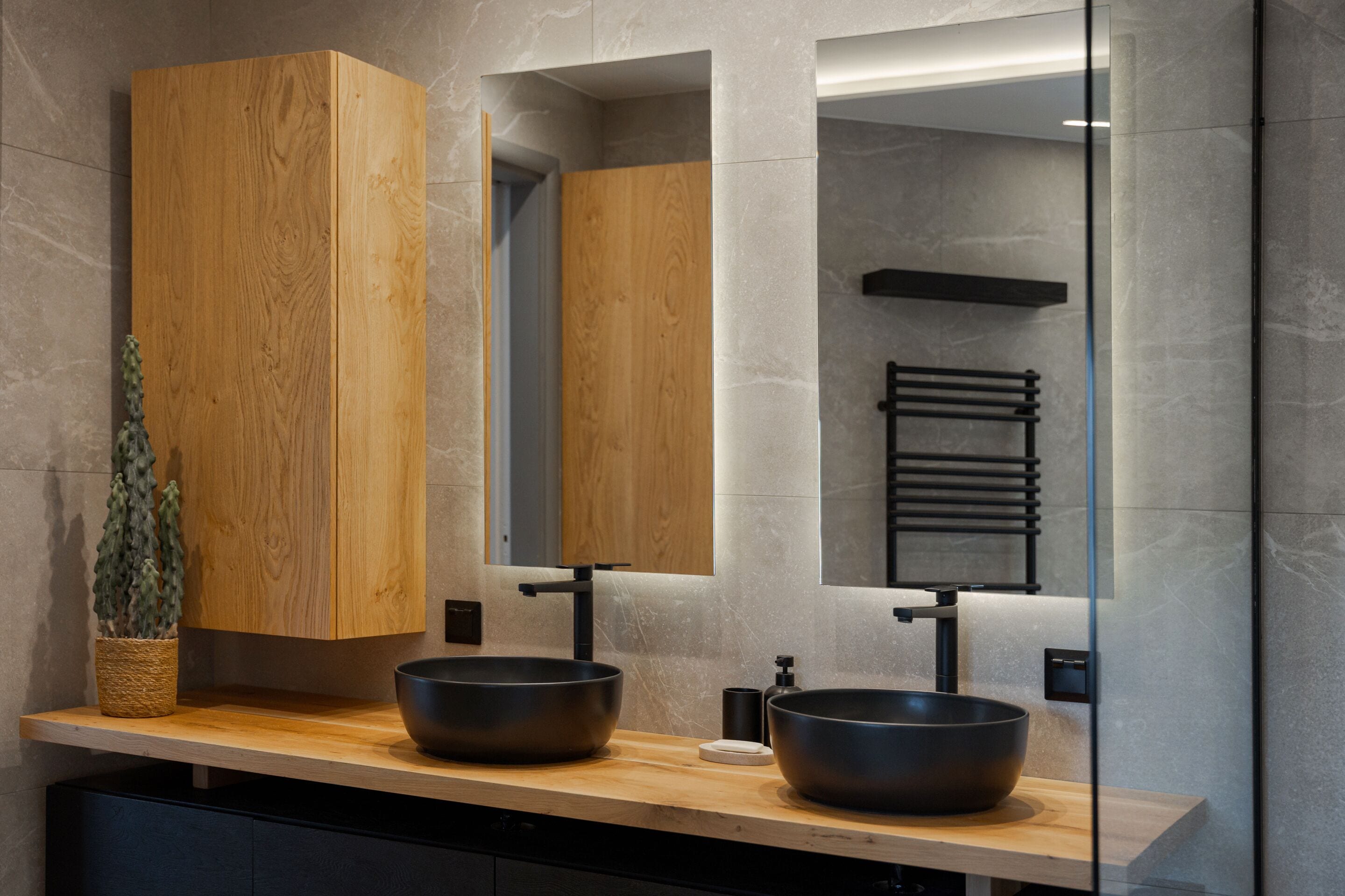A modern bathroom with a wooden vanity, two black sinks, and a large mirror.