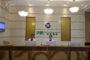 A reception desk at the WoDuBoLaI Hotel with two staff members behind it, a large logo above, and a television screen to the left. - Wodun Platinum Hotel (Qinzhou East Railway Station Niannianfeng Plaza) (Qinzhou)