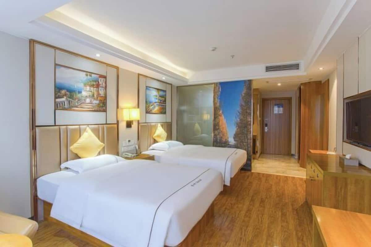 Une chambre d’hôtel avec deux lits, une télévision, un bureau et des œuvres d’art accrochées aux murs.