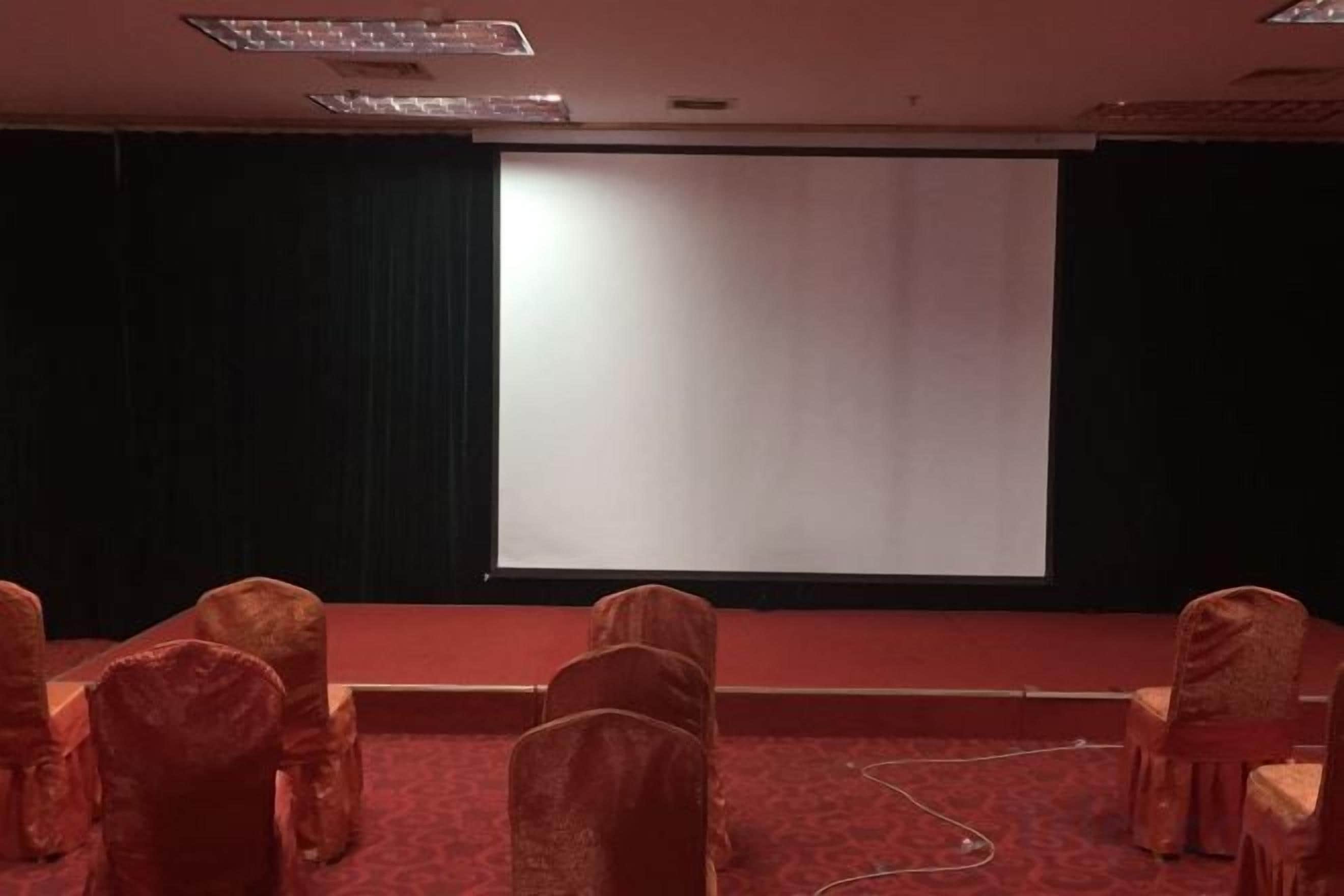 A conference room with a stage, a projector screen, and rows of chairs.