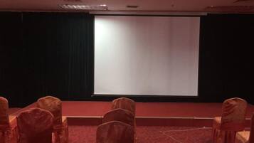 A conference room with a stage, a projector screen, and rows of chairs.
