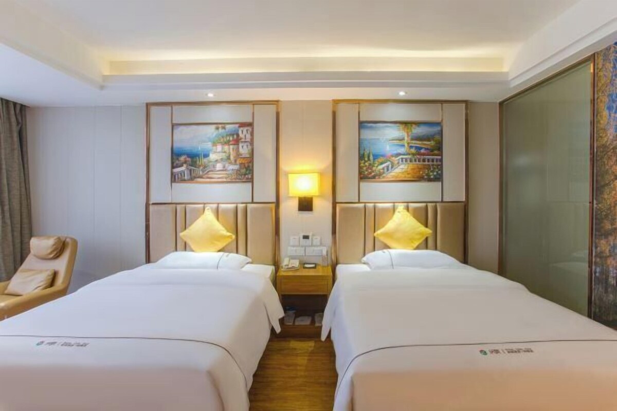 Une chambre d’hôtel avec deux lits, une chaise, une table de chevet avec une lampe et des œuvres d’art accrochées aux murs.