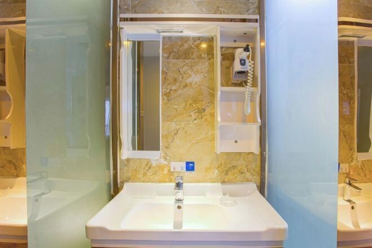 Une salle de bain avec un pare-baignoire en marbre, un lavabo, un miroir et un distributeur de serviettes.