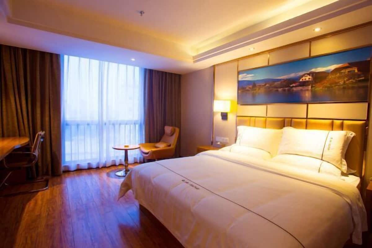 Une chambre d’hôtel avec un grand lit, un bureau, une chaise, une petite table et un tableau au mur.