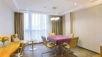 A hotel room with a dining table, chairs, a small round table, a purple tablecloth, and a large window with curtains.