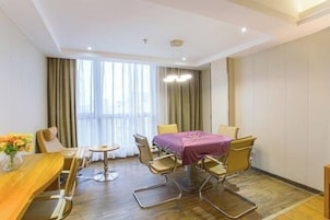 A hotel room with a dining table, chairs, a small round table, a purple tablecloth, and a large window with curtains.