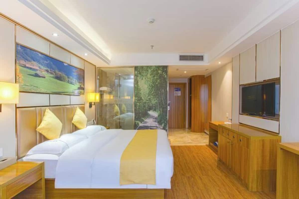 Une chambre d’hôtel avec un grand lit, une télévision, une armoire en bois et un tableau au mur.