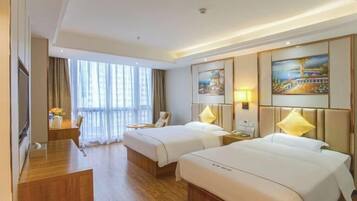 A hotel room with two beds, a desk, a chair, a TV, and large windows.