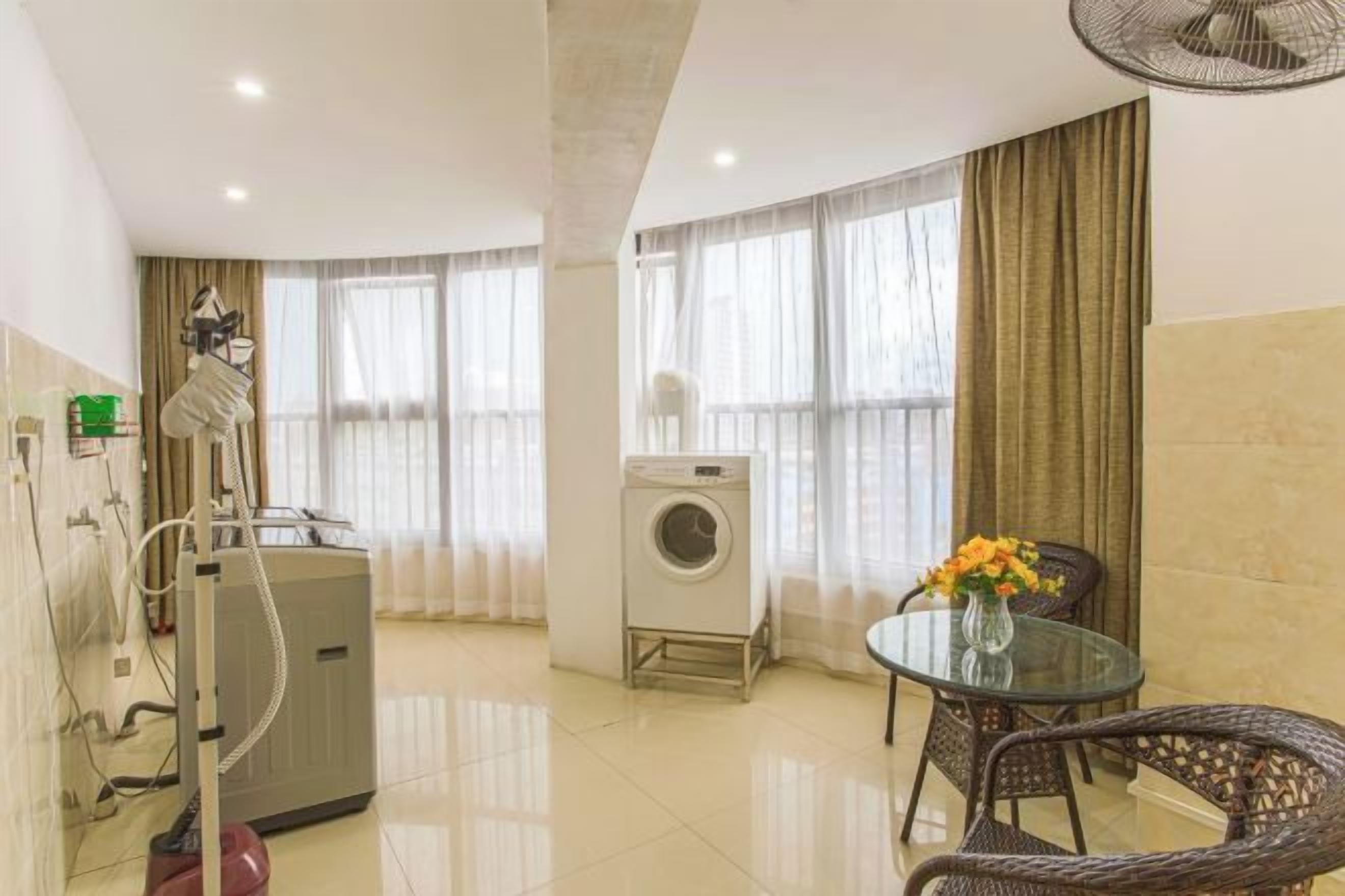 A hotel room with a bed, a washing machine, a dining table with chairs, and a fan.
