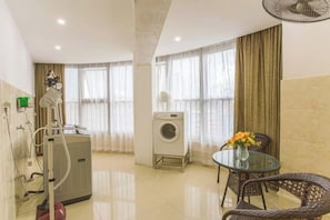 A hotel room with a bed, a washing machine, a dining table with chairs, and a fan. - Wodun Platinum Hotel (Qinzhou East Railway Station Niannianfeng Plaza) (Qinzhou)