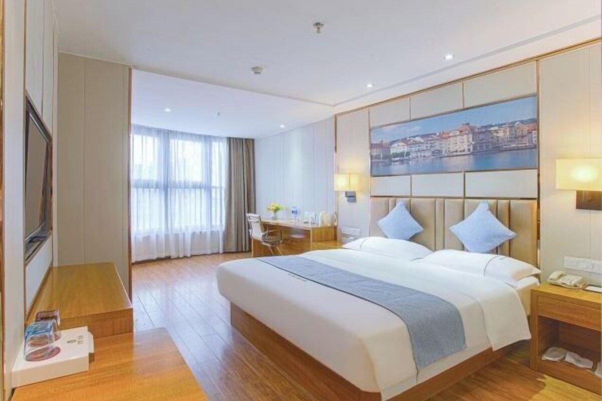 Une chambre d’hôtel avec un grand lit, un bureau et une vue sur le paysage urbain par la fenêtre.