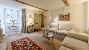 Un salon avec un canapé beige, une table basse, un tapis à motifs, une lampe et un tableau au mur.