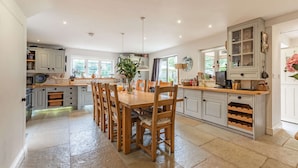 A spacious kitchen with a large dining table, wooden chairs, and a built-in island with a sink and storage. - Impressive five bedroom country home in the Cotswolds - Barnsley Cottage (Cirencester)