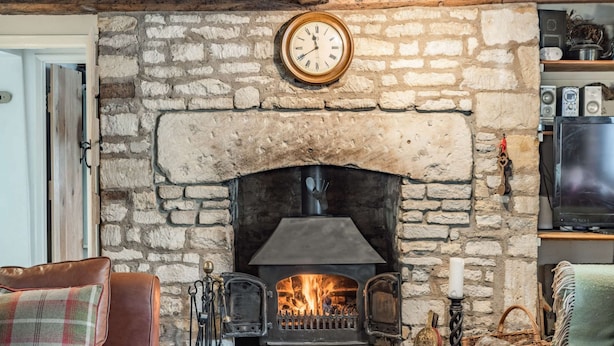 A stone fireplace with a clock above it, a television on the right, and a cozy seating area with a plaid throw pillow. - Impressive five bedroom country home in the Cotswolds - Barnsley Cottage (Cirencester)