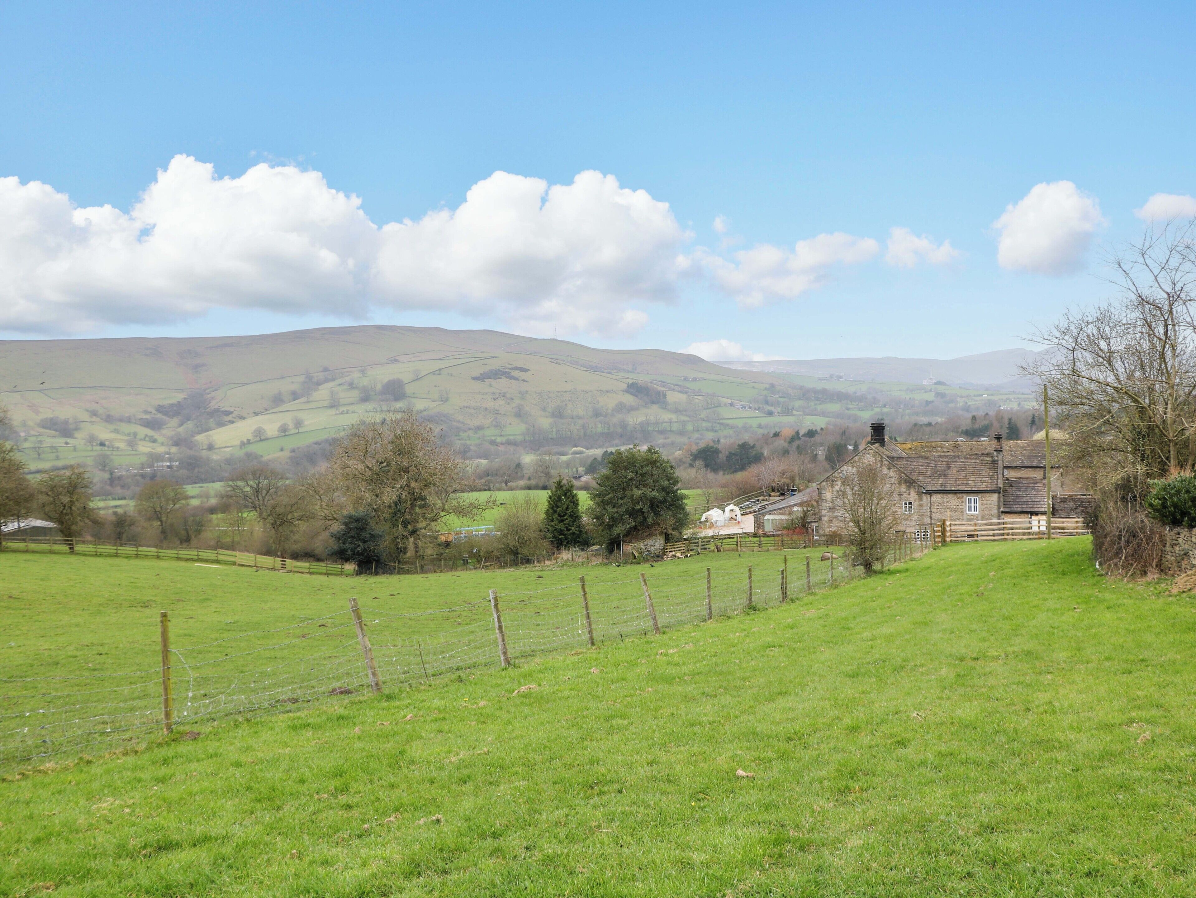 A rural landscape with a stone house, green fields, and rolling hills in the background.