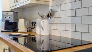 A kitchen with a coffee maker, kettle, and utensils on the counter. - 18th century thatched Cotswold holiday cottage in Broadway - Orchard Cottage, Broadway (Broadway)